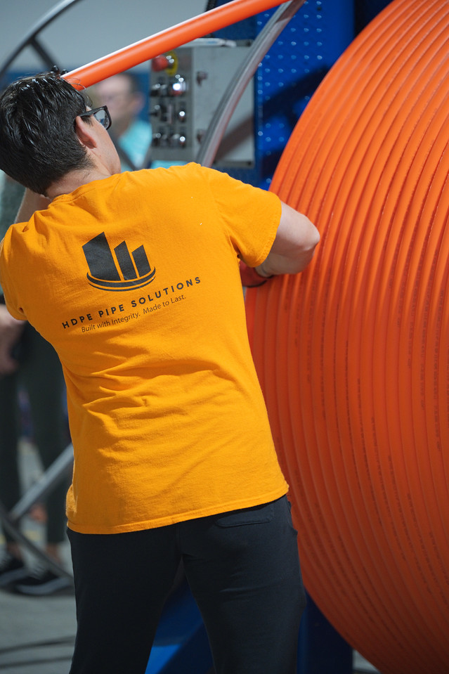A team member on the production floor in an HDPE Pipe Solutions shirt reading Built with Integrity, Made to Last