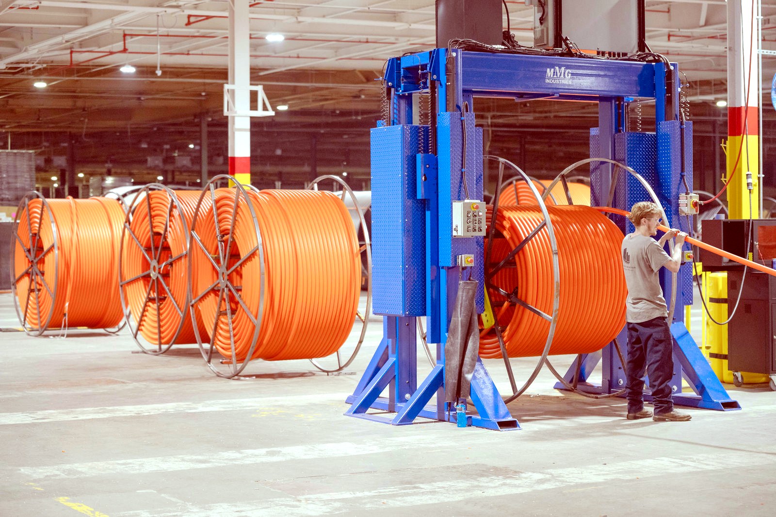 A team member running the take-up winder with reels of orange HDPE conduit staged on the production floor